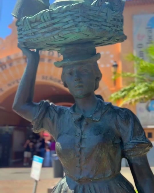 Statua in bronzo di una donna con cesto in una piazza storica acciottolata